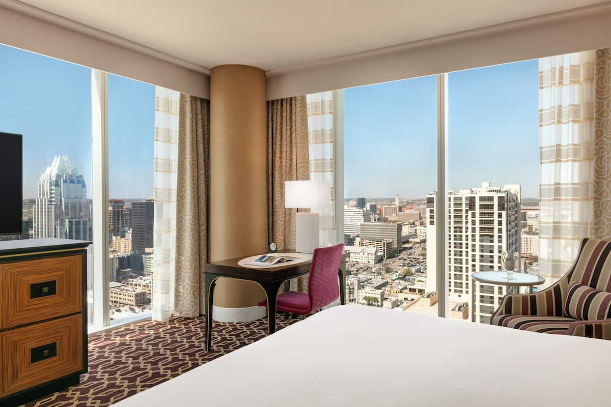 A hotel room with a large bed, a desk with a chair, a TV, and a view of a cityscape.