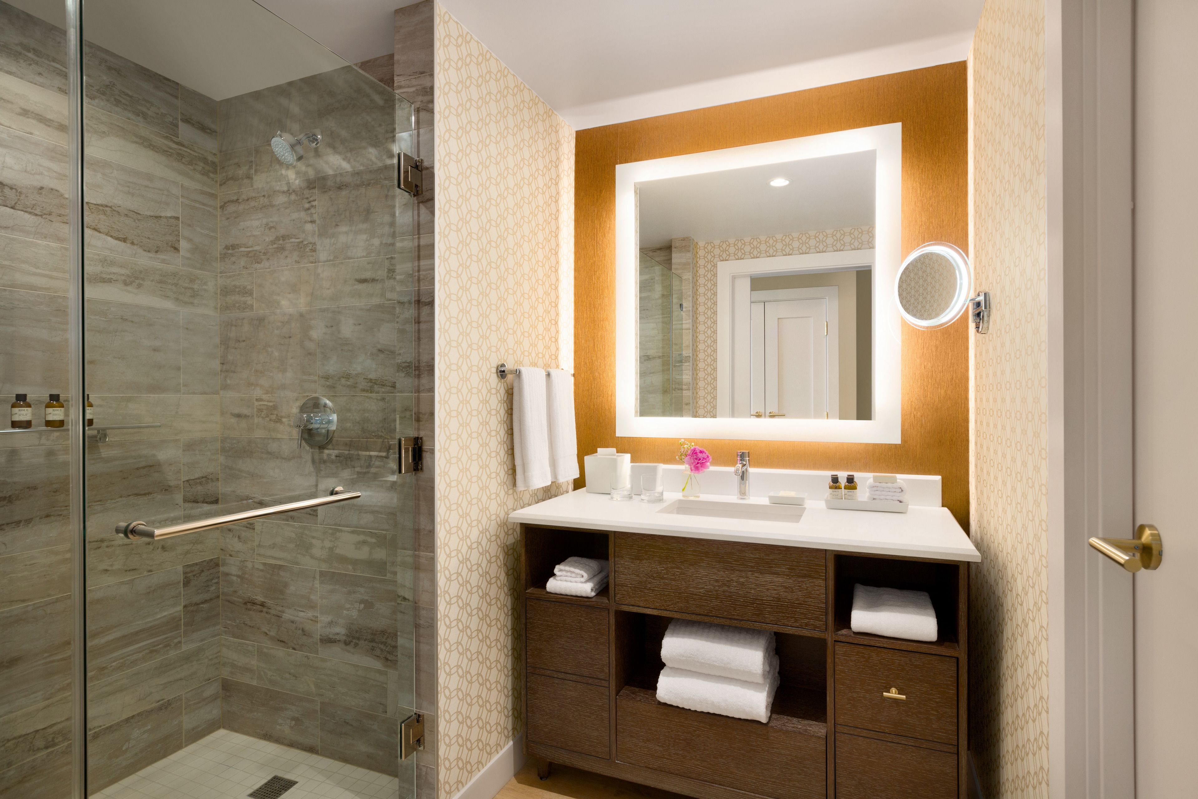 A bathroom with a glass shower enclosure, a vanity with a mirror, and a sink.