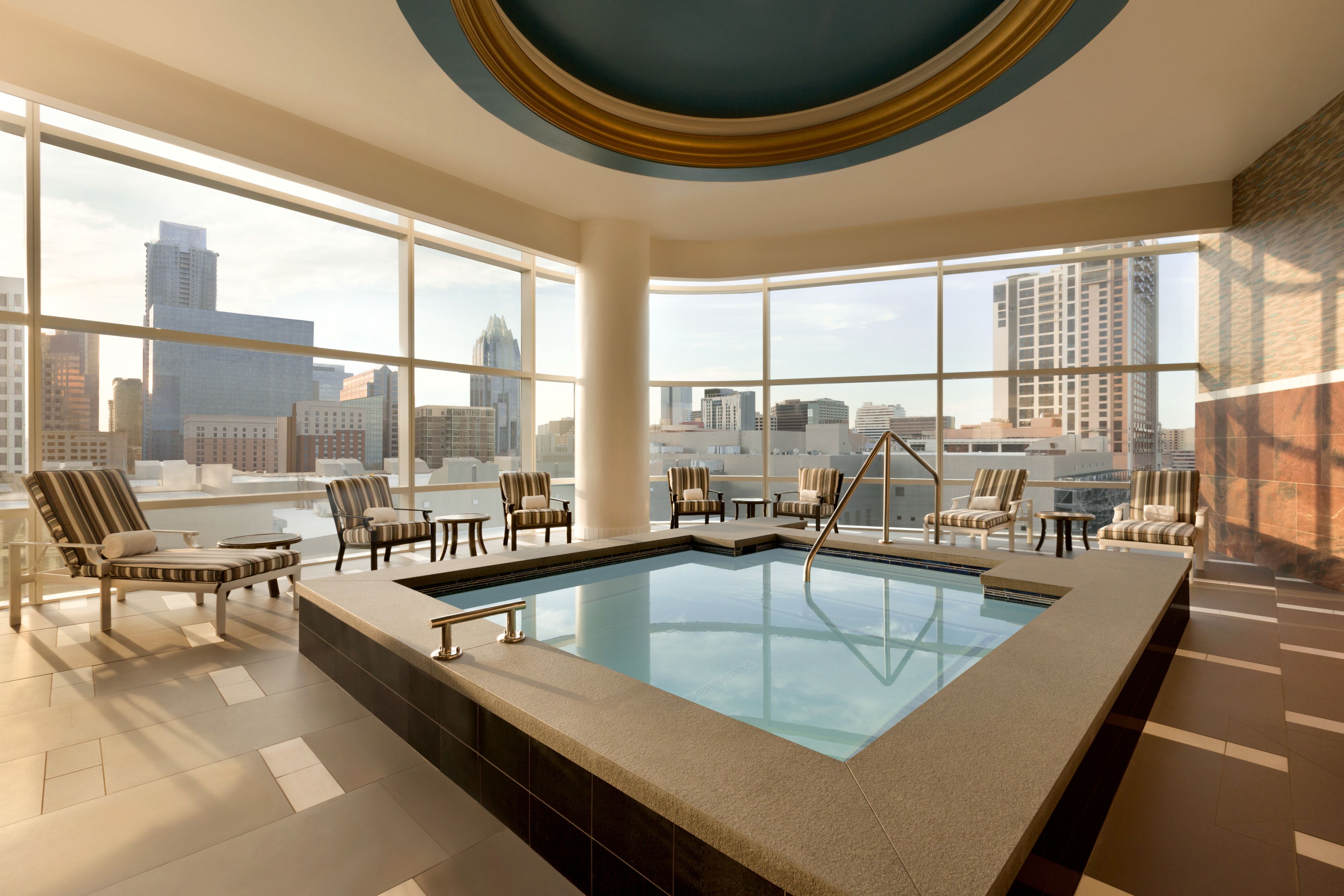 Piscina infinita en la azotea con vistas a la ciudad, sillas de descanso y un diseño interior moderno.