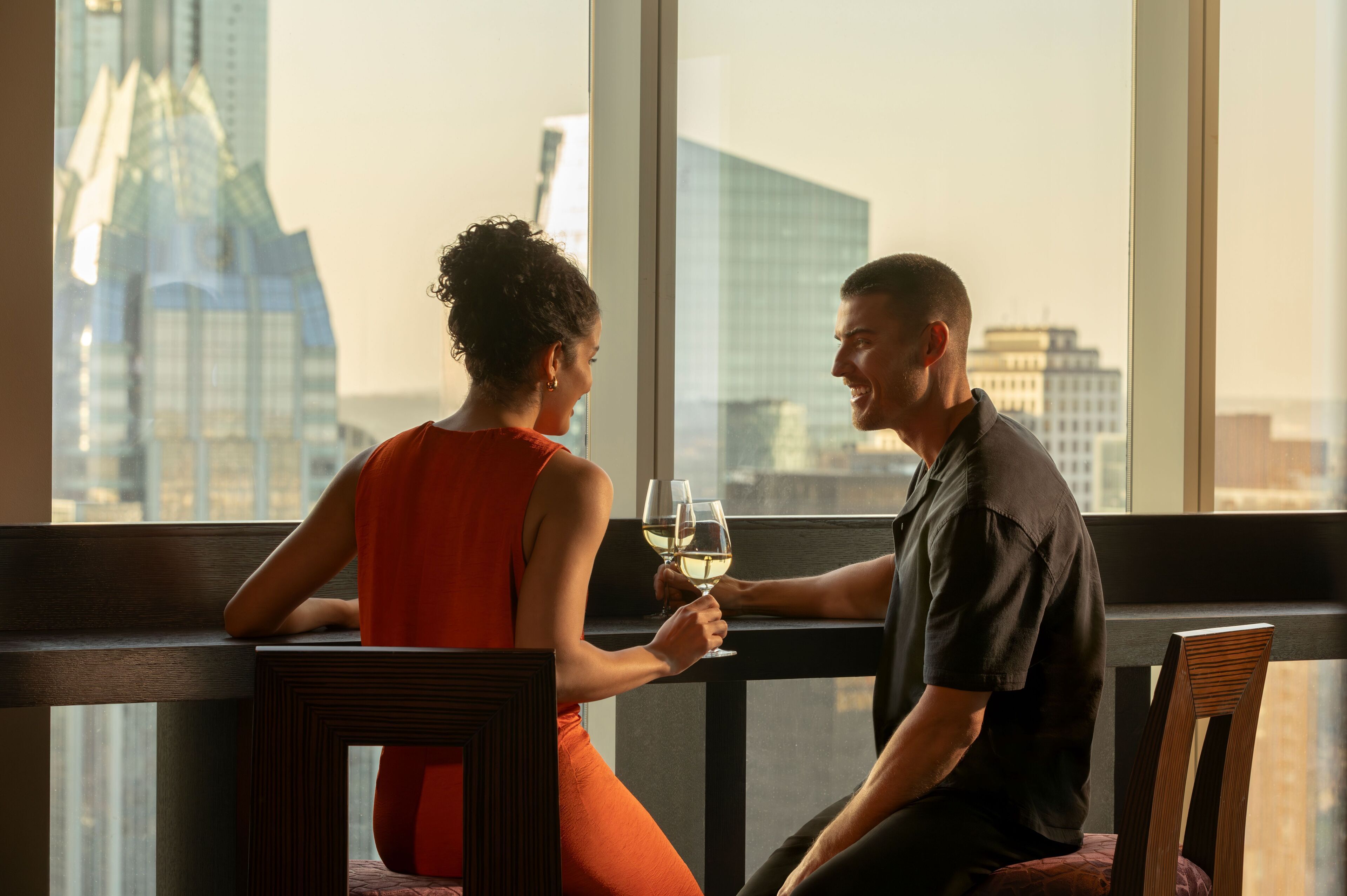 A couple sitting at a table with a city view, holding wine glasses.