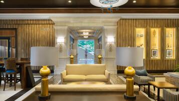 A lobby with a sofa, two lamps, a chandelier, and a staircase leading to another area.