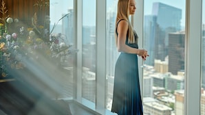 Une femme se tient près d’une grande fenêtre, d’où l’on peut admirer le paysage urbain.