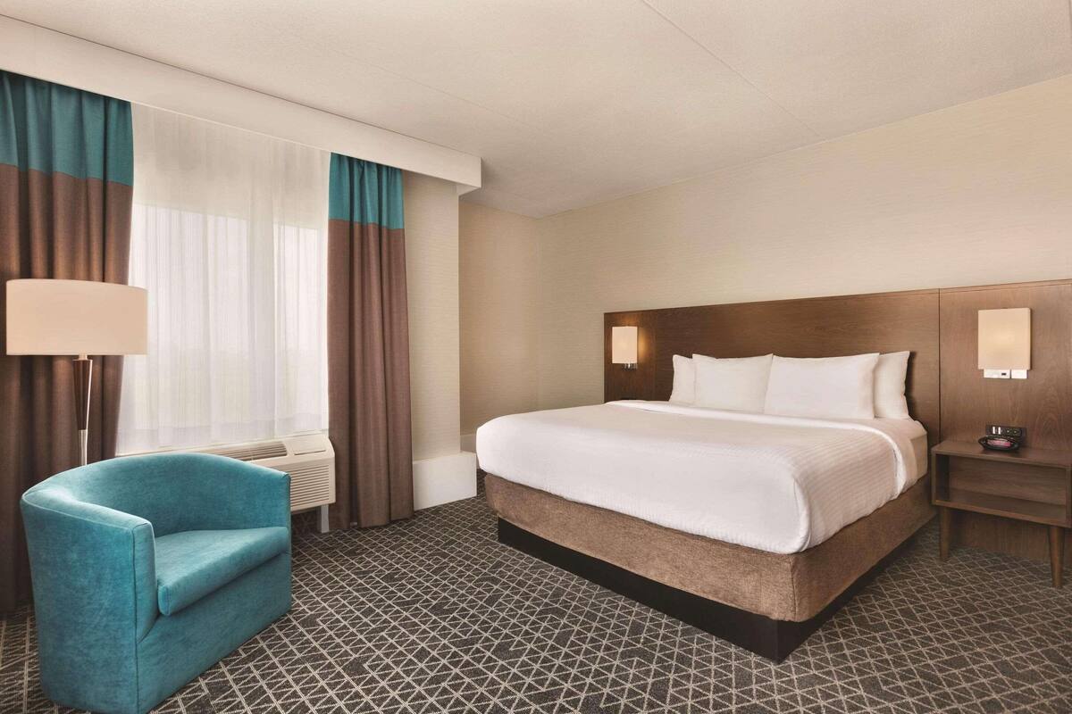 A hotel room with a bed, a chair, a nightstand, and a lamp.