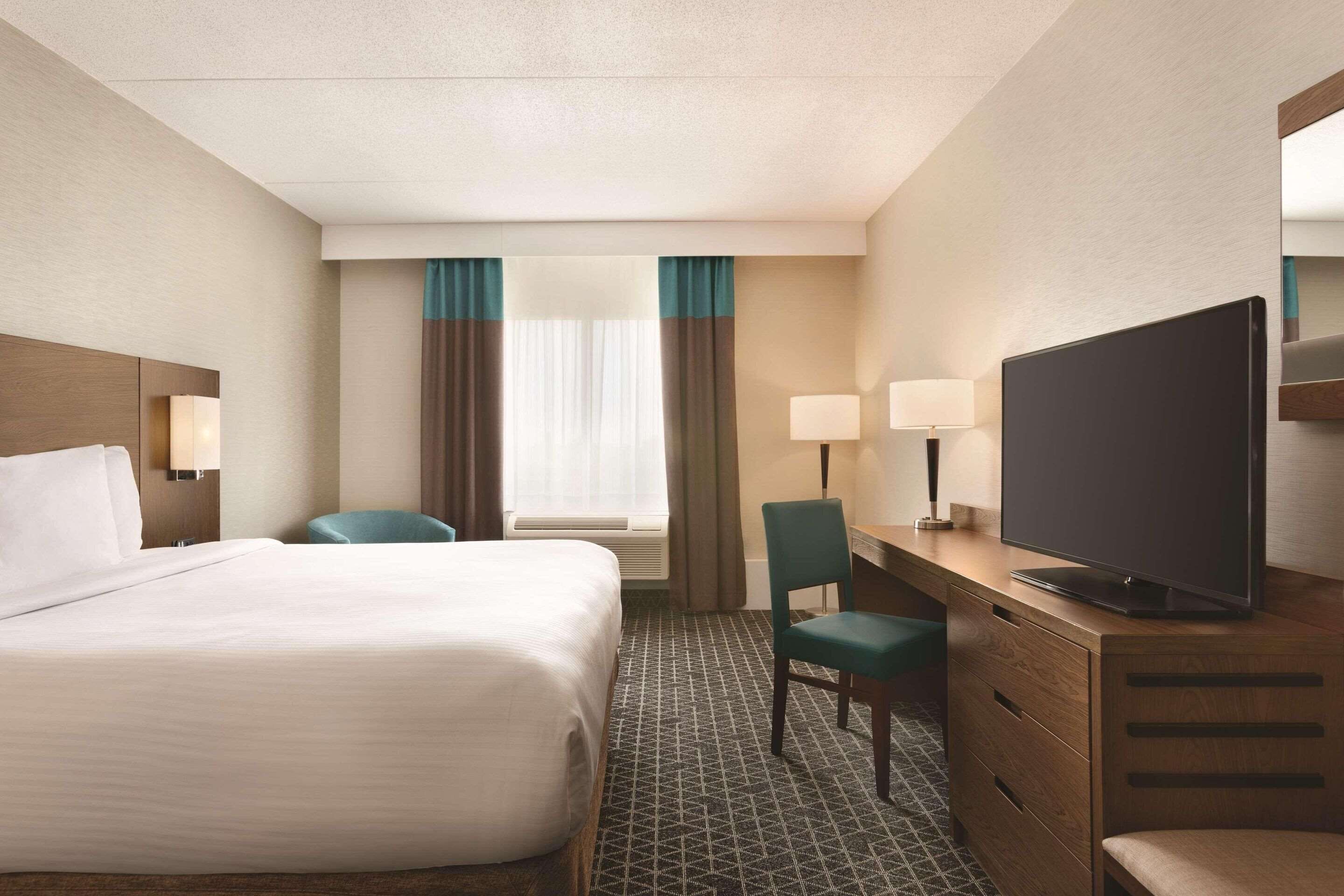 A hotel room with a large bed, a desk with a television, and a chair.