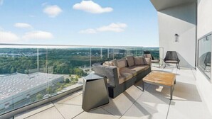 A modern balcony with a sofa, chairs, and a coffee table, overlooking a cityscape.