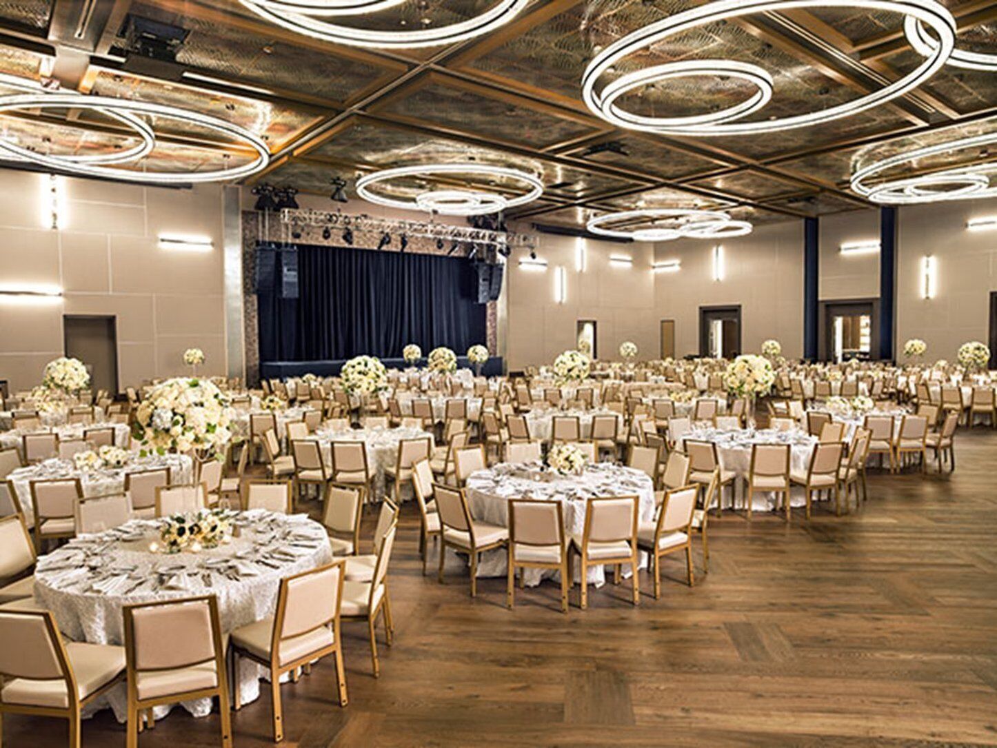 A banquet hall with round tables, chairs, and floral centerpieces.