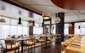 A spacious restaurant with high ceilings, pendant lighting, and a mix of seating arrangements including tables and booths.