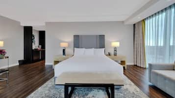 Un hotel moderno con una cama grande, mesitas de noche, un banco y vistas a la ciudad a través de amplias ventanas.