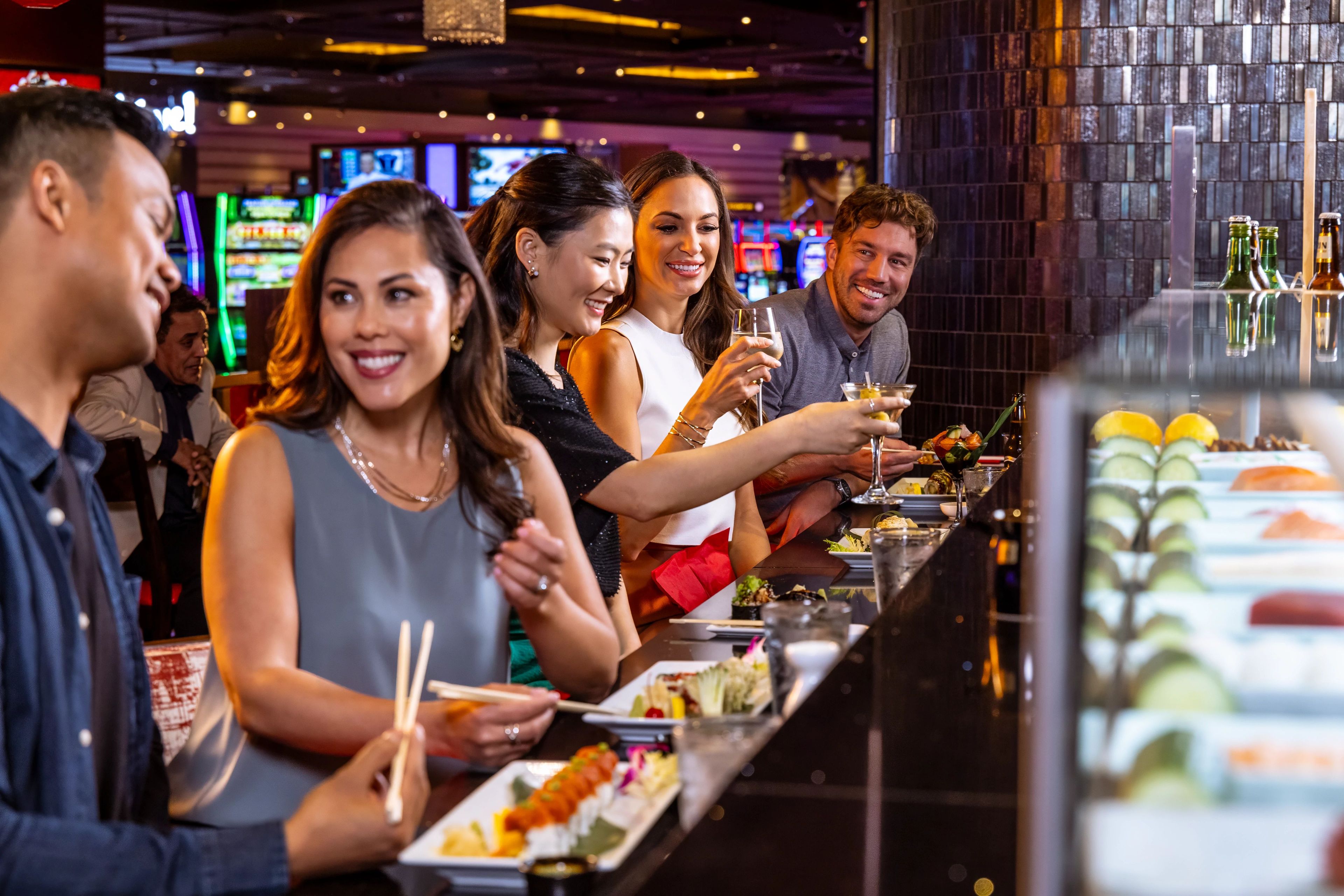 Eine Gruppe von Menschen speist an einer Bar mit Sushi und Cocktails.