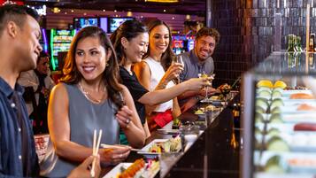 Eine Gruppe von Menschen speist an einer Bar mit Sushi und Cocktails.
