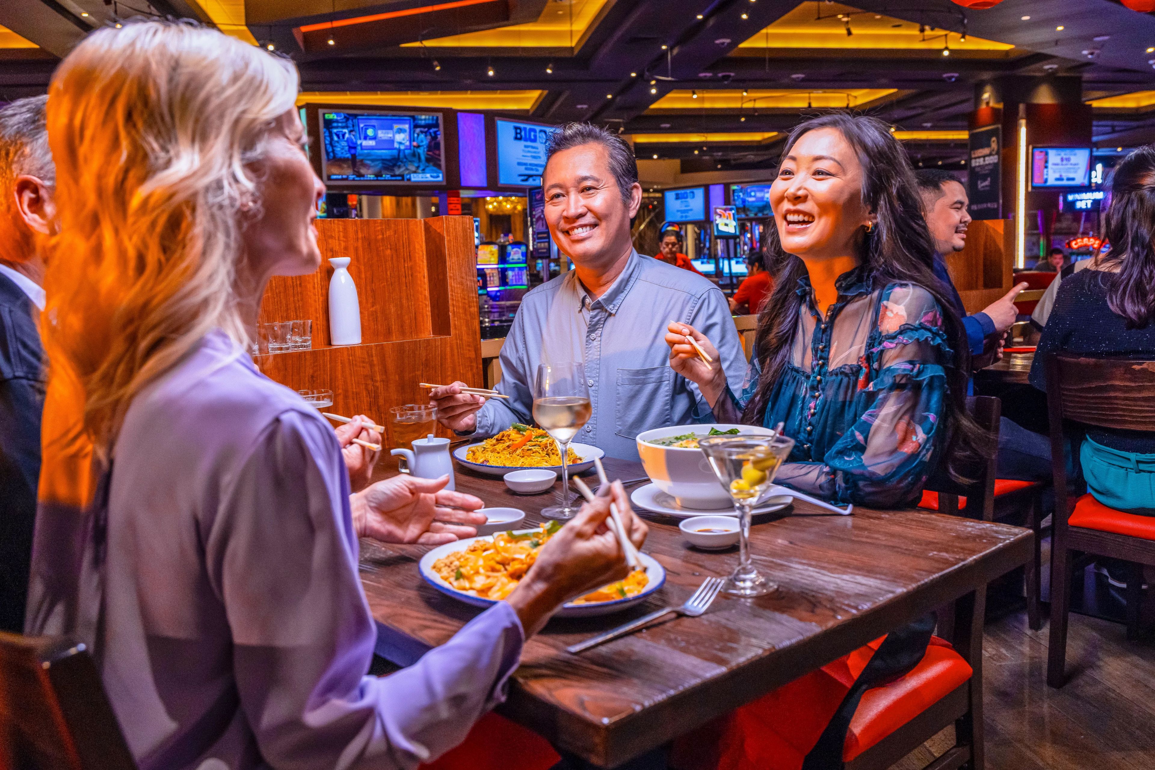 A group of people dining at a restaurant with multiple screens in the background.