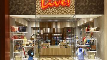 Moderni myymälä, jossa on suuri ja näkyvästi sijoitettu kyltti, jossa lukee ”SHOP Live!”, lasivitriinit ja kuvioitu lattia.