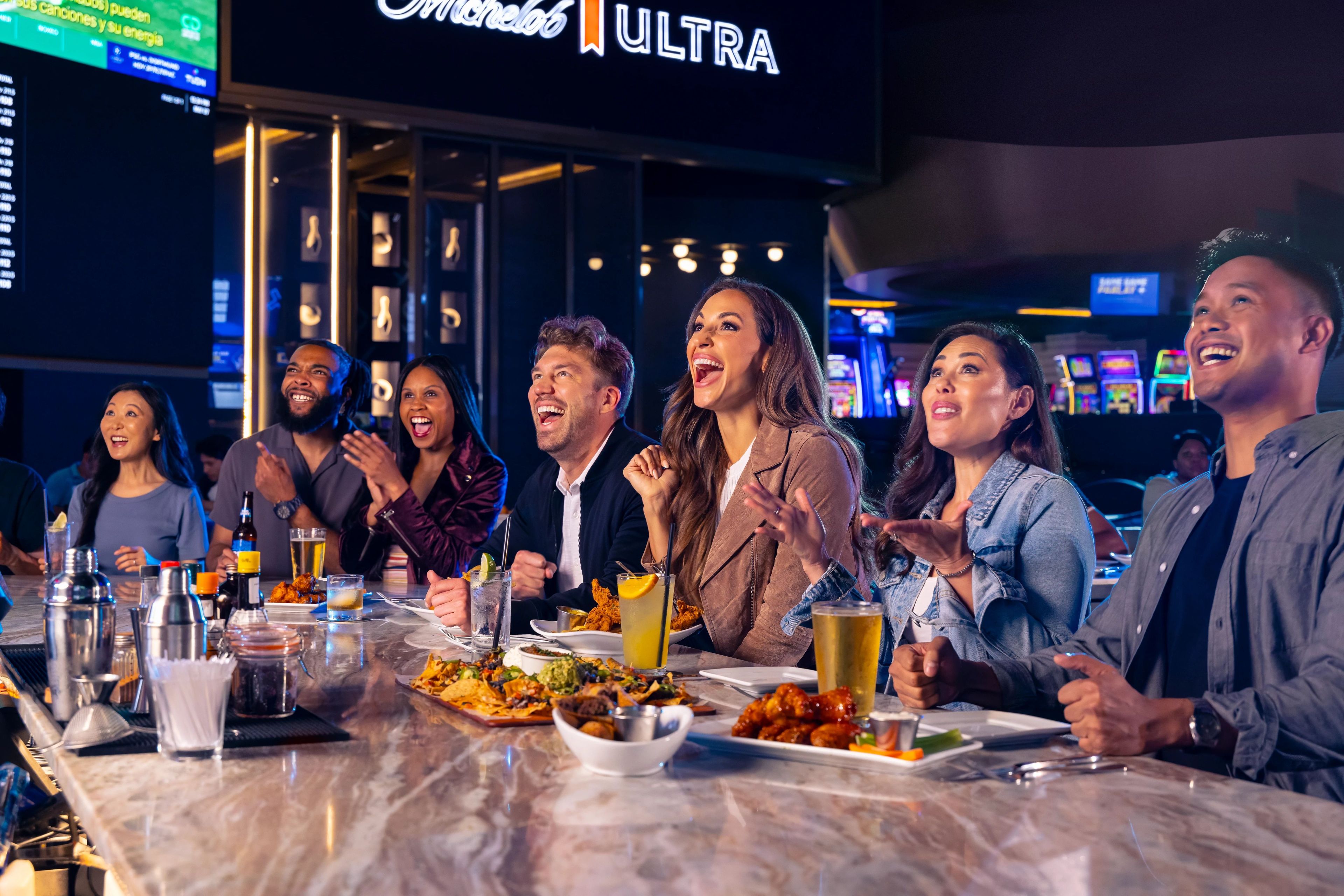 Un grupo de personas sentadas en un bar, con un letrero de neón al fondo.