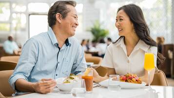 A couple dining in a restaurant with a table set for two, a glass of orange juice, and a variety of dishes.