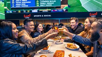 A group of people toasting at a bar with a sports display in the background.