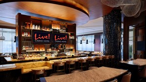 A bar area with multiple liquor bottles, a 'Live! Casino Hotel' sign, and bar stools. - Live! Casino & Hotel Maryland (Hanover)