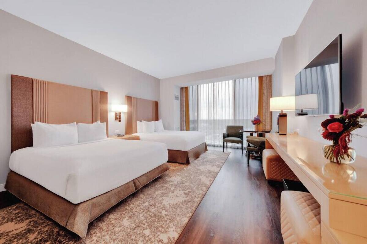 A hotel room with two beds, a desk, a chair, a TV, and a window with curtains.