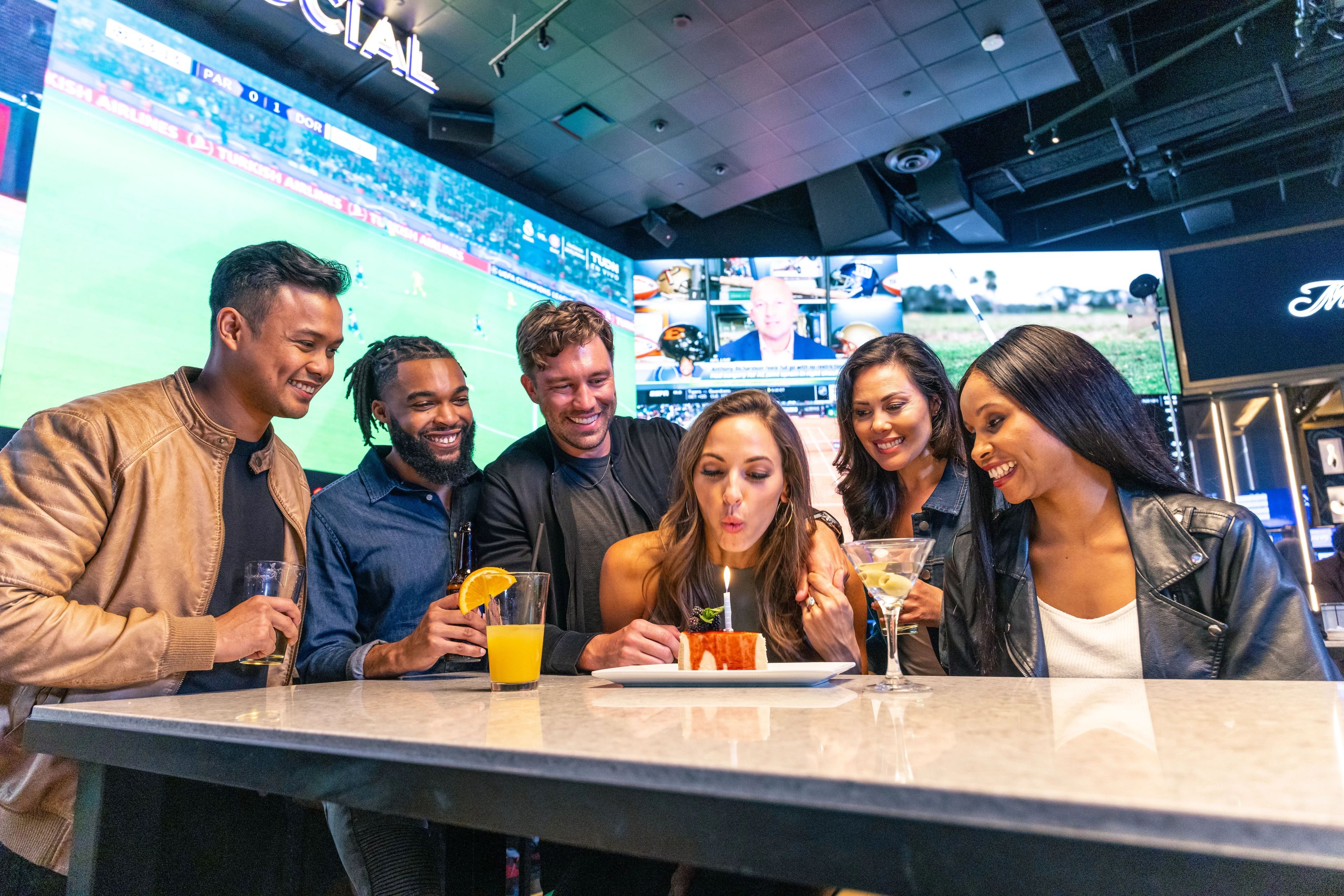 Un grup de persones a un bar amb una televisió que mostra esports al fons.
