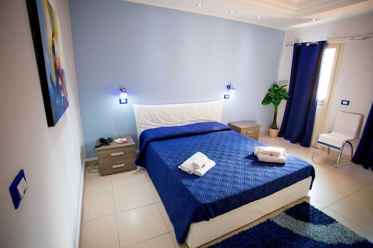 A bedroom with a bed, bedside tables, a potted plant, and a chair.