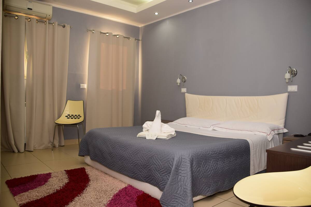 A bedroom with a bed, a chair, a nightstand, and a lamp.