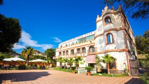 A historic building with a courtyard, outdoor seating, and palm trees. - Palace Hotel Costa Del Sole (Catania)