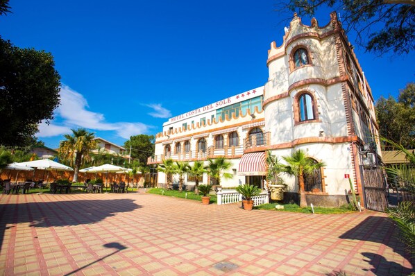 A historic building with a courtyard, outdoor seating, and palm trees.