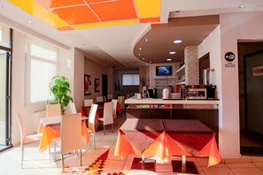 A modern restaurant with a bar area, seating, and a television screen. - Palace Hotel Costa Del Sole (Catania)