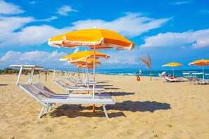 A beach with rows of sun loungers and orange umbrellas. - Palace Hotel Costa Del Sole (Catania)