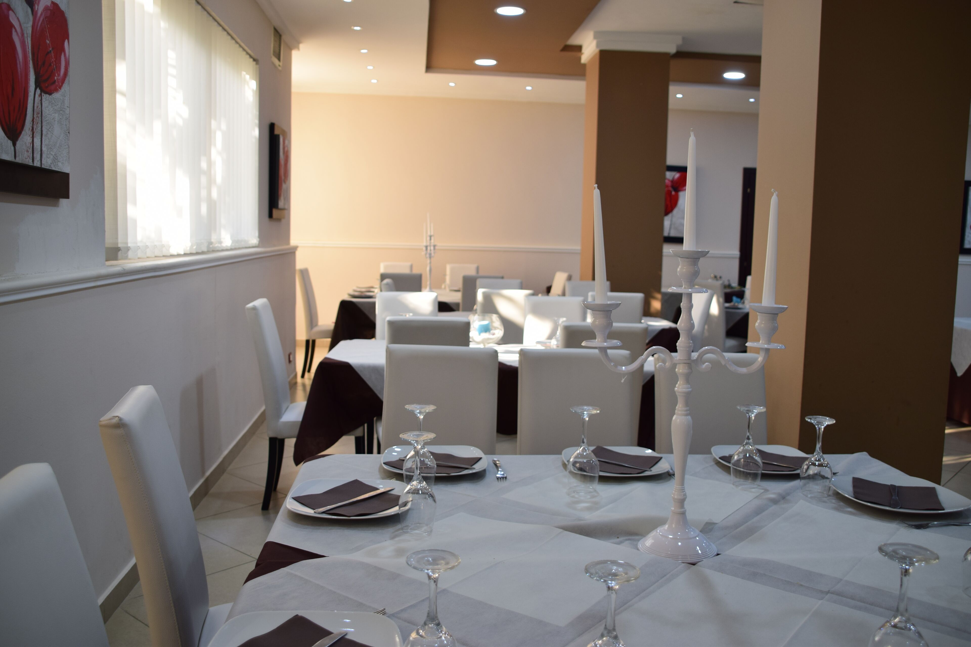 A dining area with tables set for a meal, white chairs, and candle holders.