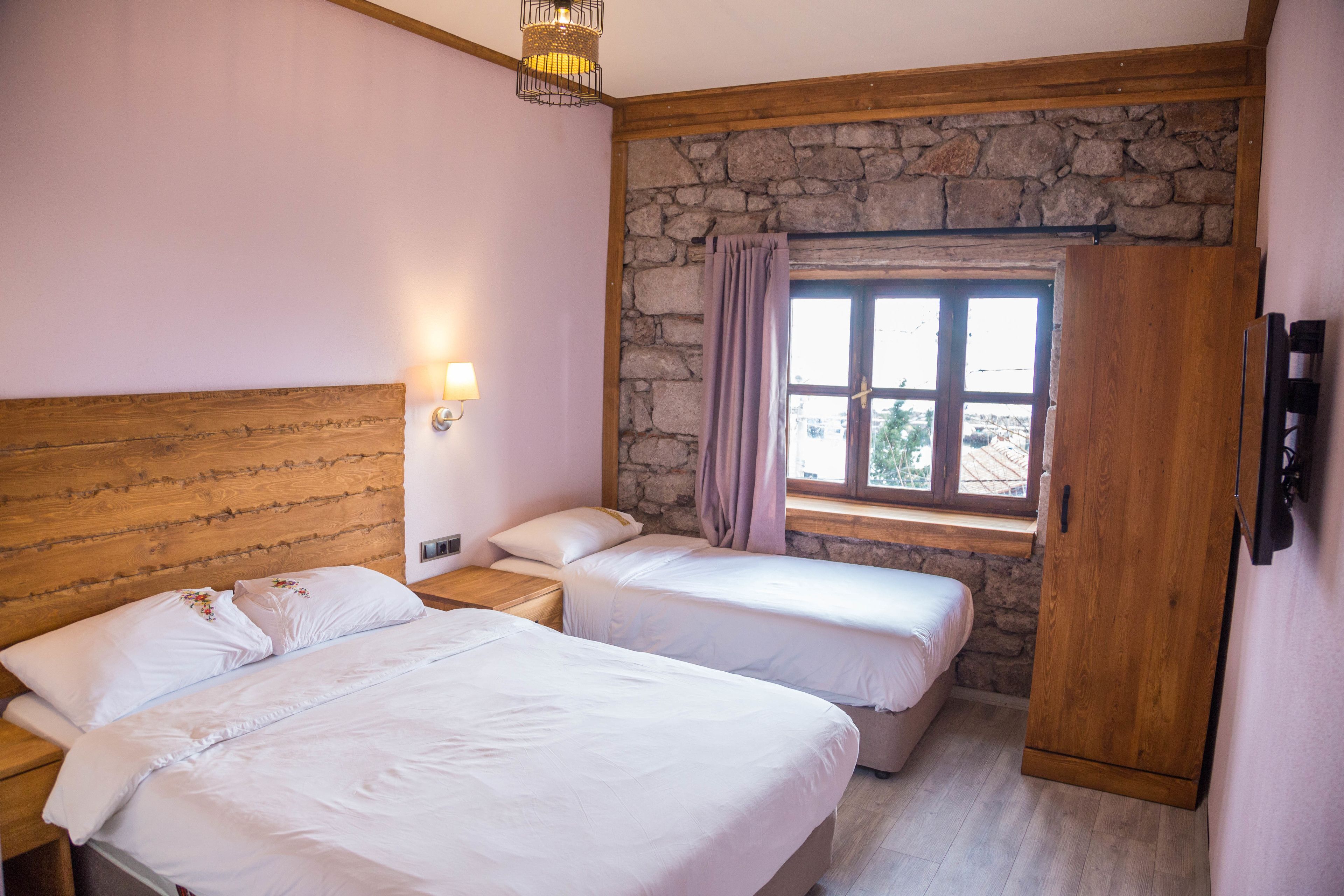 Una camera da letto con due letti, una parete in pietra, una finestra con tende, un armadio in legno e un comodino con una lampada.