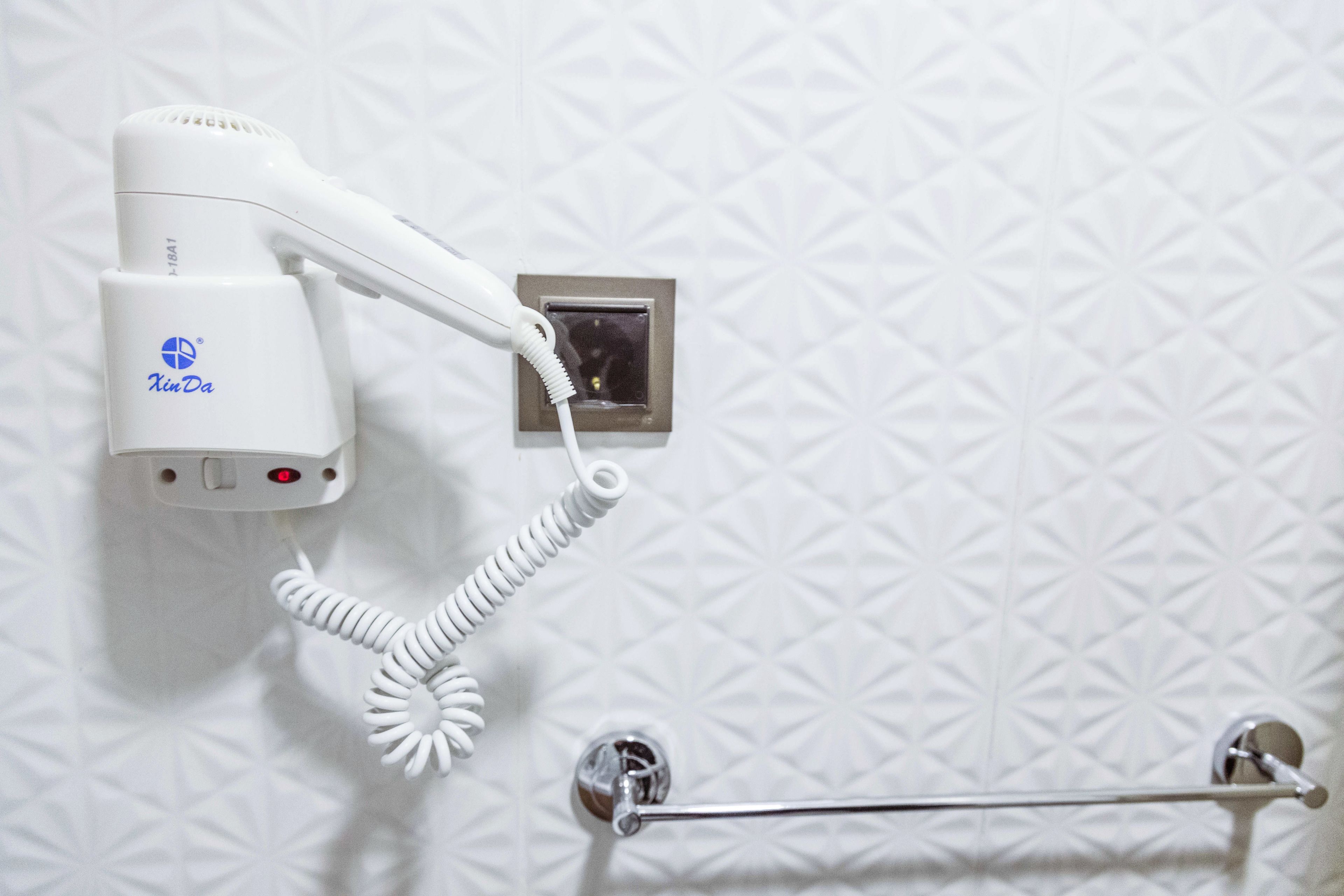 Un secador de pelo fijado en una pared con textura y un perchero debajo.