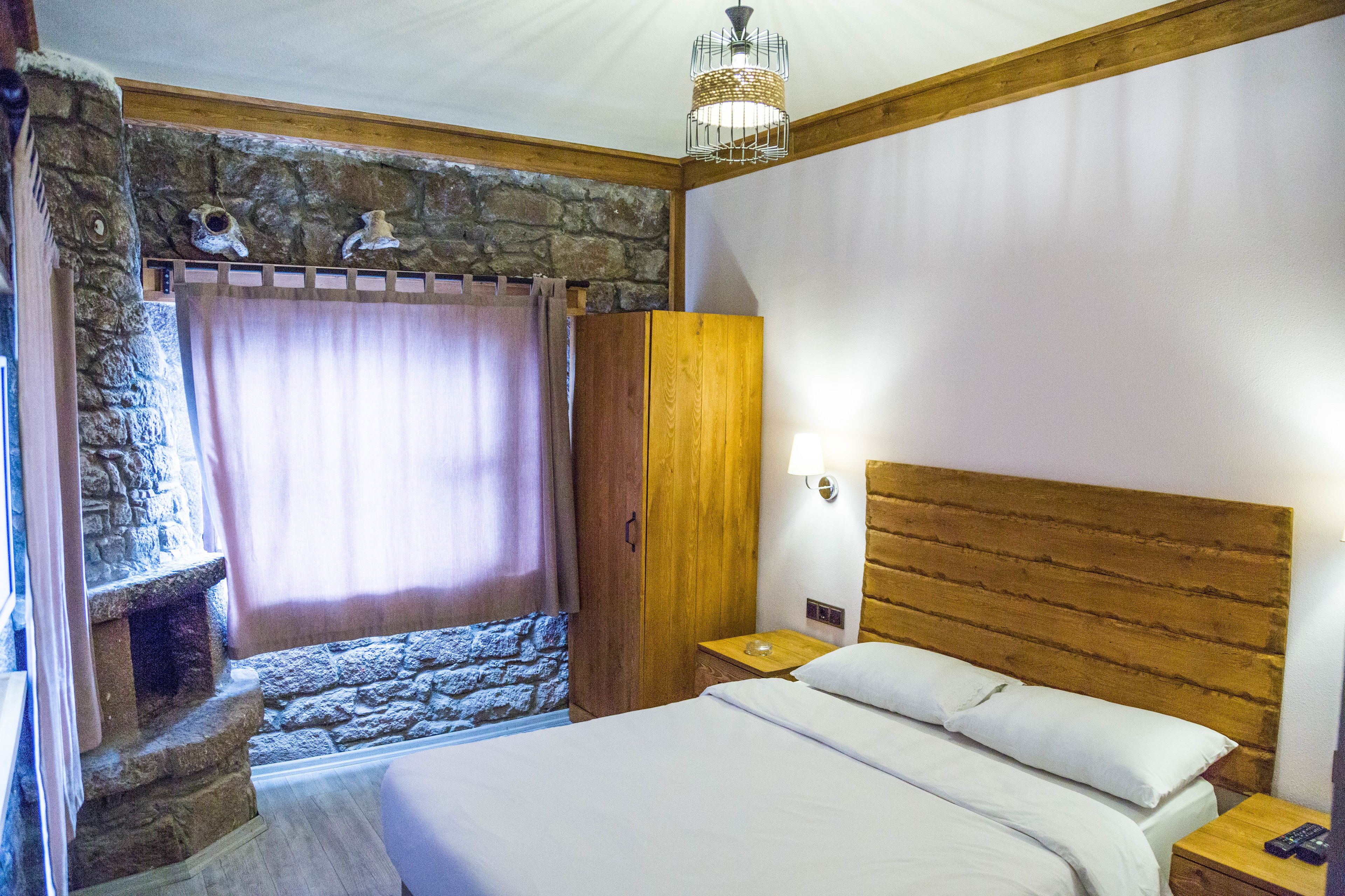 A bedroom with a stone wall, wooden headboard, and a bed with white linens.