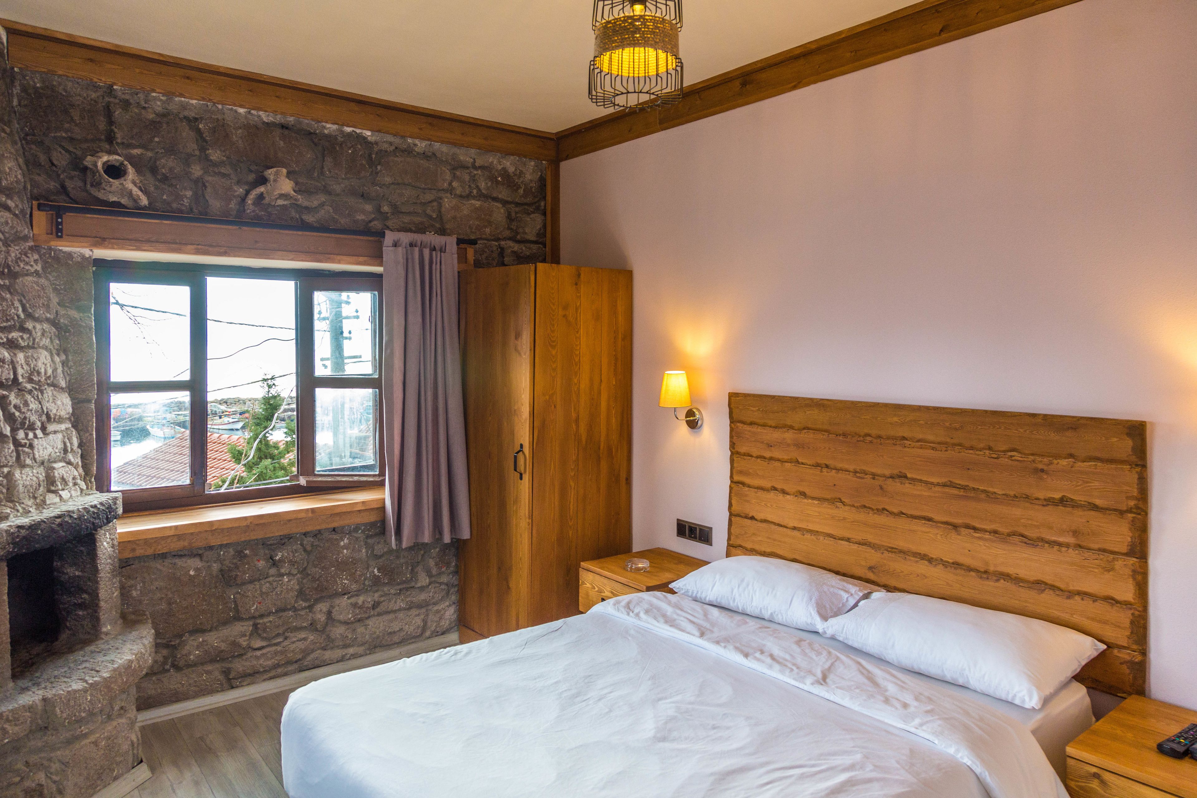 A bedroom with a stone fireplace, wooden headboard, and a nightstand with a lamp.