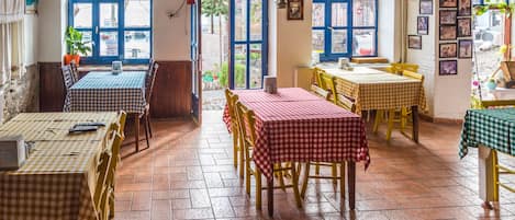 A restaurant with multiple tables and chairs, a tiled floor, and a view of the street through large windows.