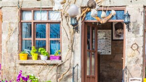 A rustic stone building with a wooden door, potted plants on the windowsill, and hanging decorations. - Assos Yildiz Hotel (Ayvacik)