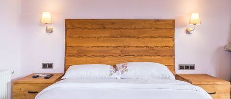 Una cama bien hecha con sábanas blancas y almohadas estampadas, flanqueada por mesitas de noche de madera con lámparas, en una habitación con cabecera de madera y paredes de tonos claros.