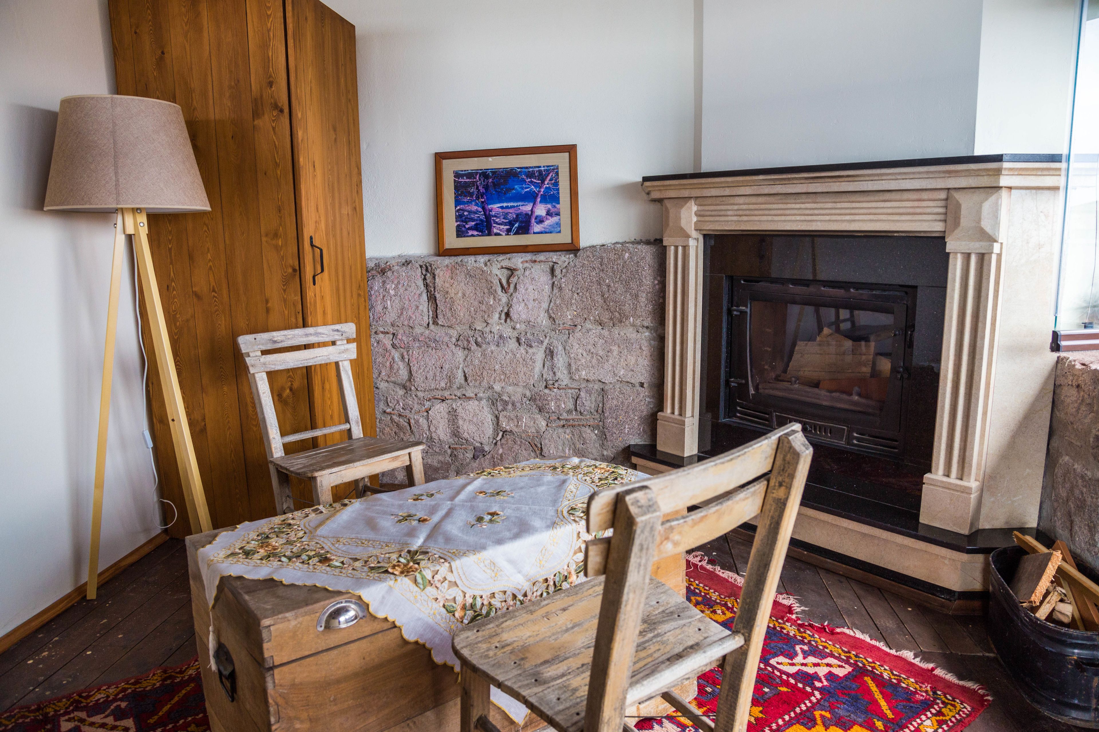 A cozy room with a stone fireplace, a wooden table with a tablecloth, a wooden chair, and a floor lamp.