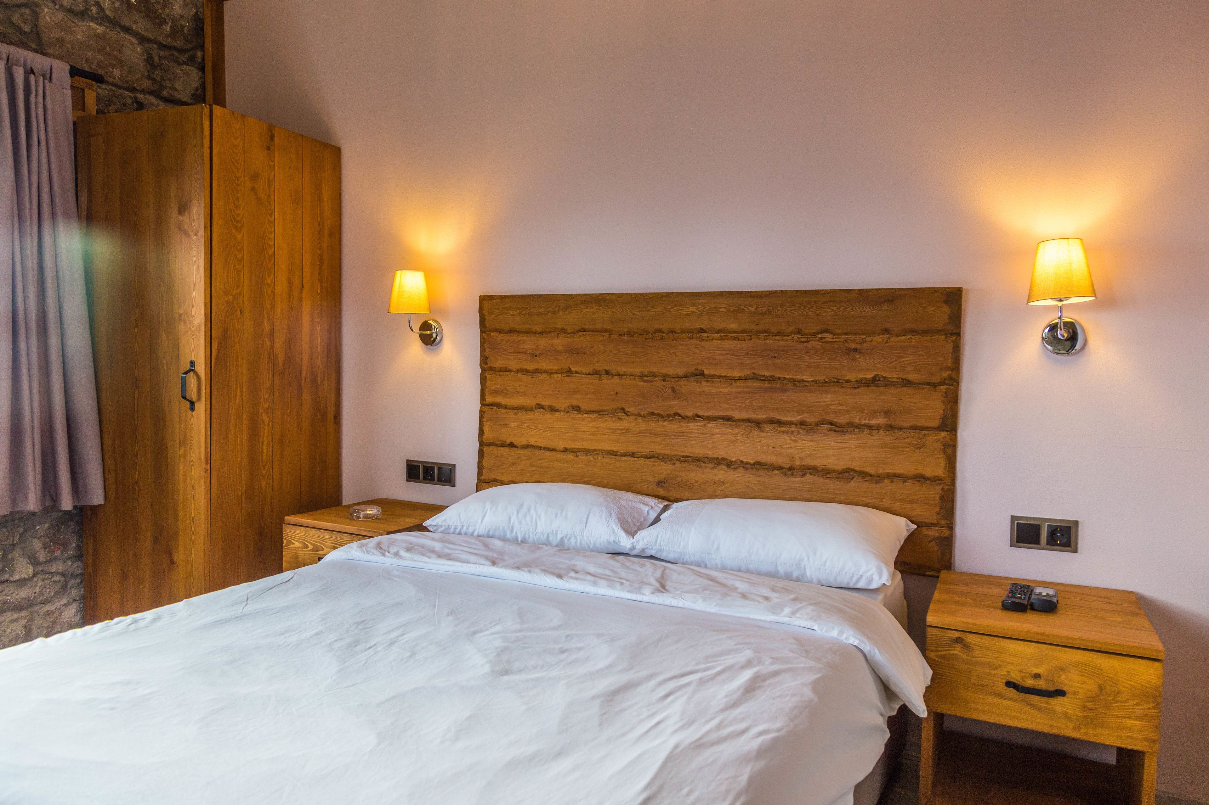 Una cama bien hecha con sábanas blancas, cabecera de madera, dos mesitas de noche con lámparas y un armario de madera.