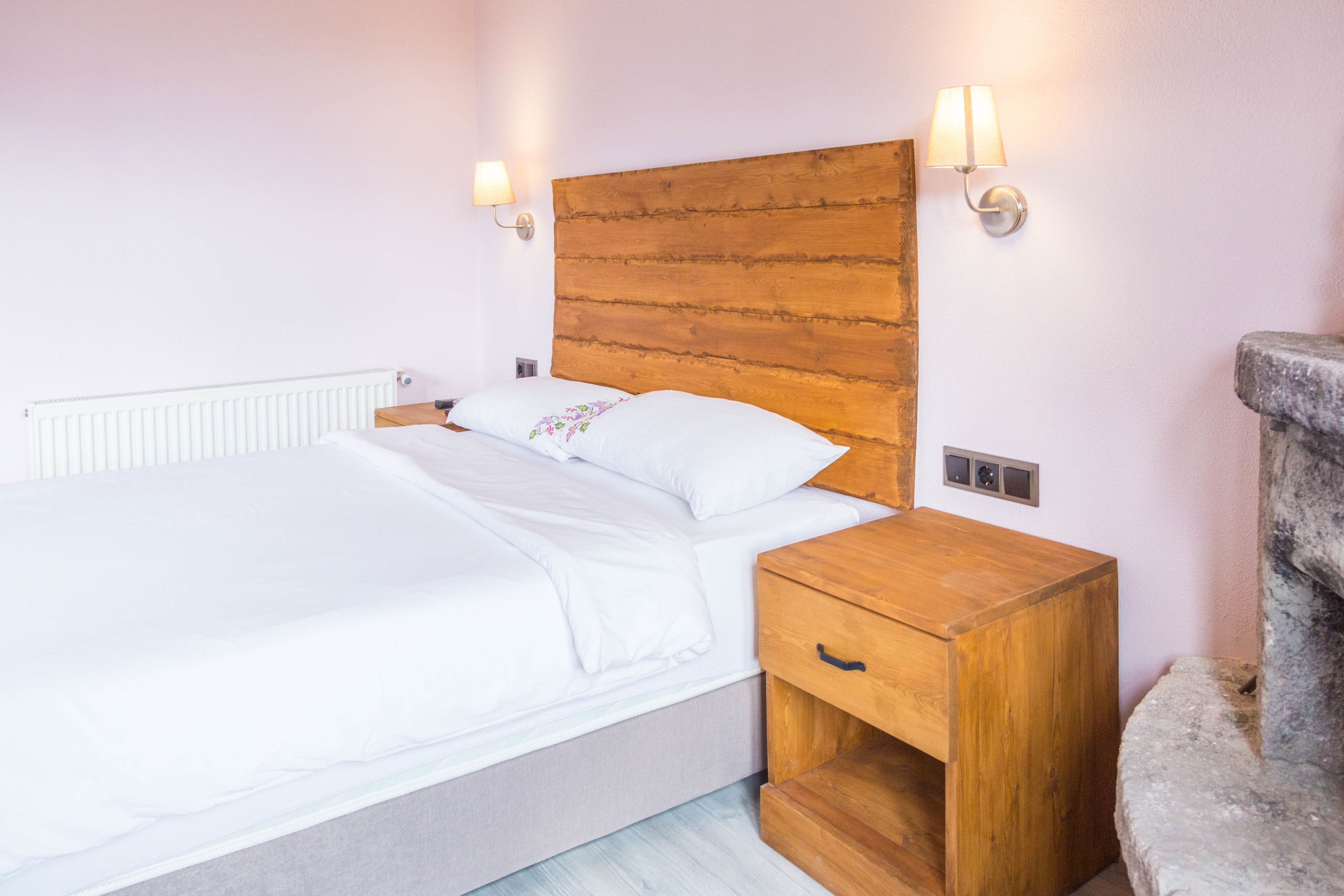 Una cama con cabecera de madera, lámparas de noche y una mesita de noche con cajón.
