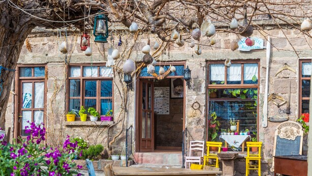 A rustic stone building with a wooden table and chairs outside, potted plants, and hanging decorative items. - Assos Yildiz Hotel (Ayvacik)