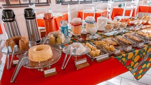 Una mesa de buffet con diversos alimentos y utensilios, que incluye un pastel, productos de repostería y una estación de café.