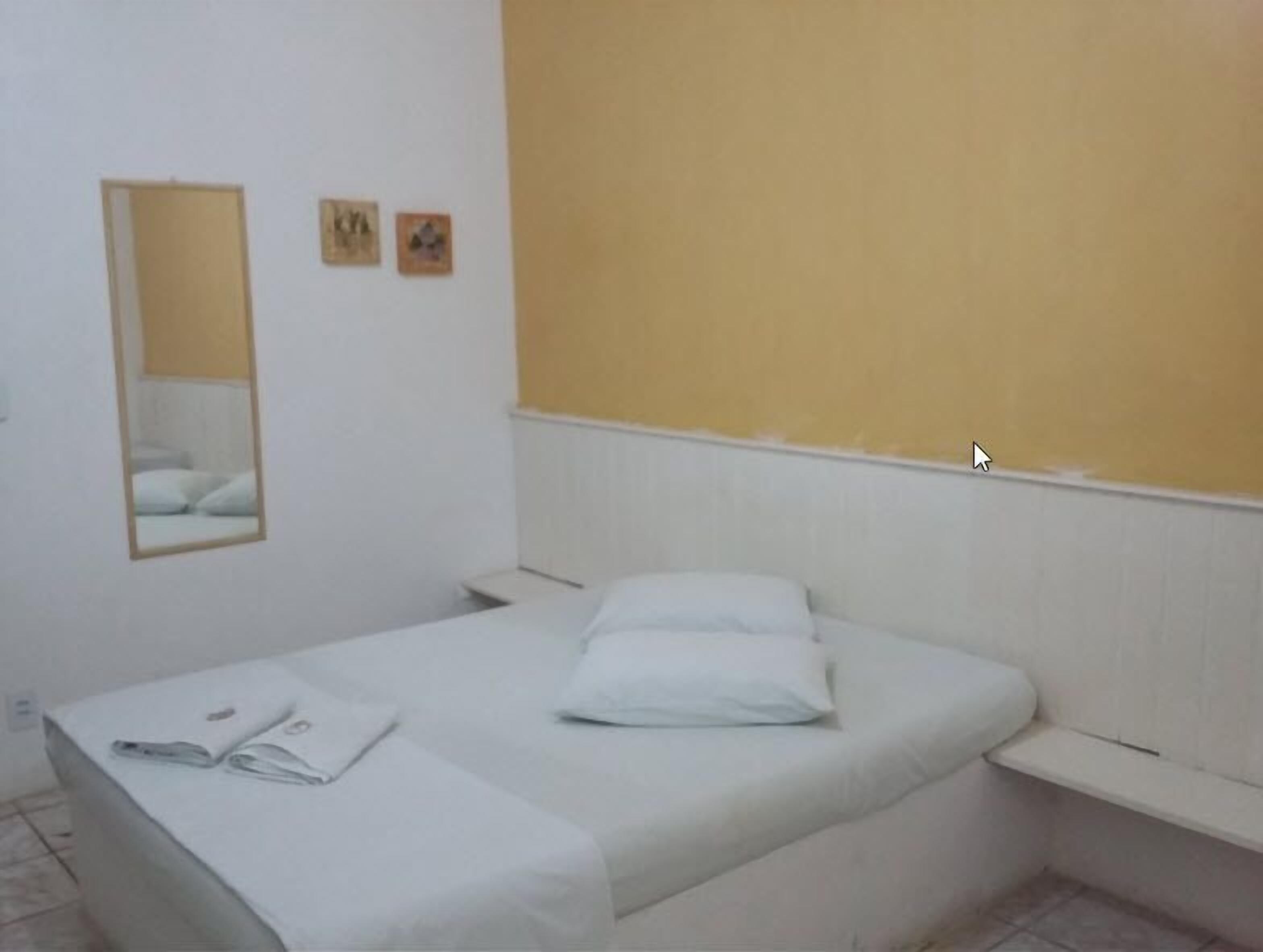 Una habitación pequeña con una cama individual, una mesita de noche, un espejo y un estante sencillo.