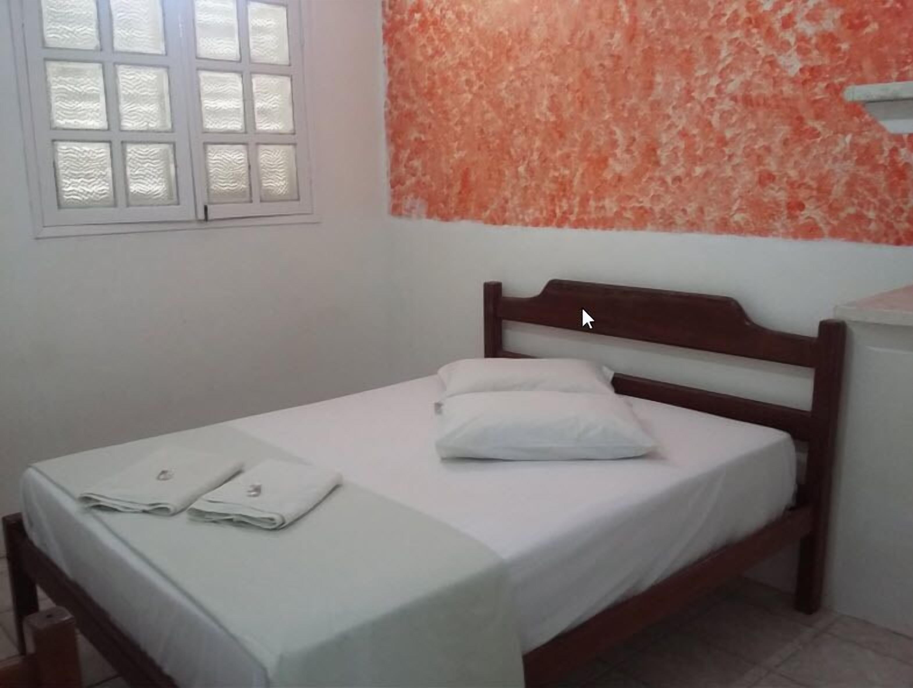 A single bed with a wooden headboard, a white mattress, and two neatly folded white towels.