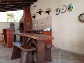 A rustic outdoor kitchen with a brick oven, wooden table, and benches. - Pousada Pé de Caju (Alcobaca)