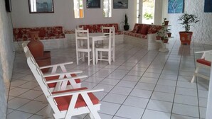 Un salón amplio con suelo de baldosas, un conjunto de sofás, una mesa de comedor con sillas y varias plantas en macetas.