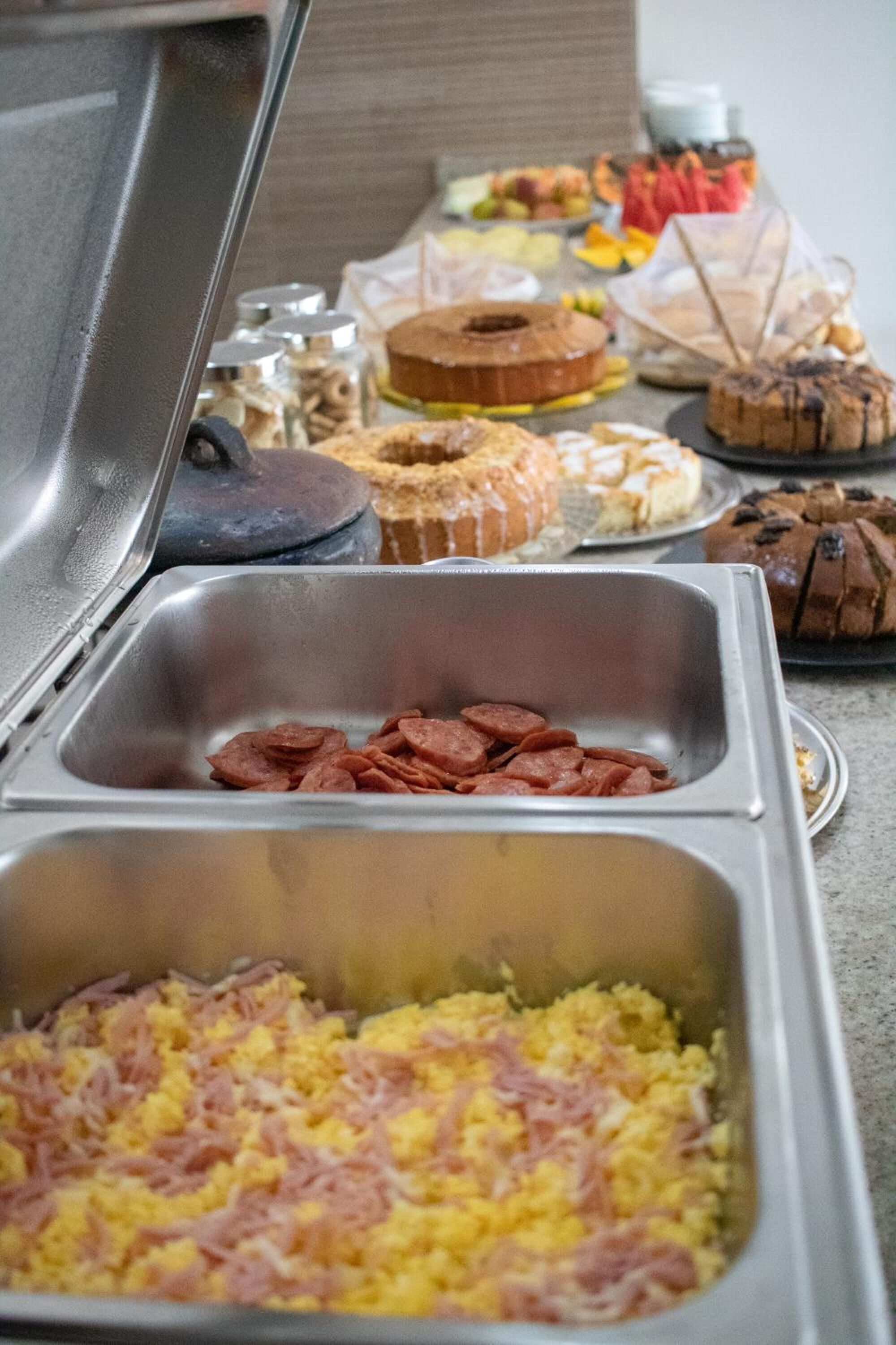 A buffet with various food items including scrambled eggs, sausage, and pastries.