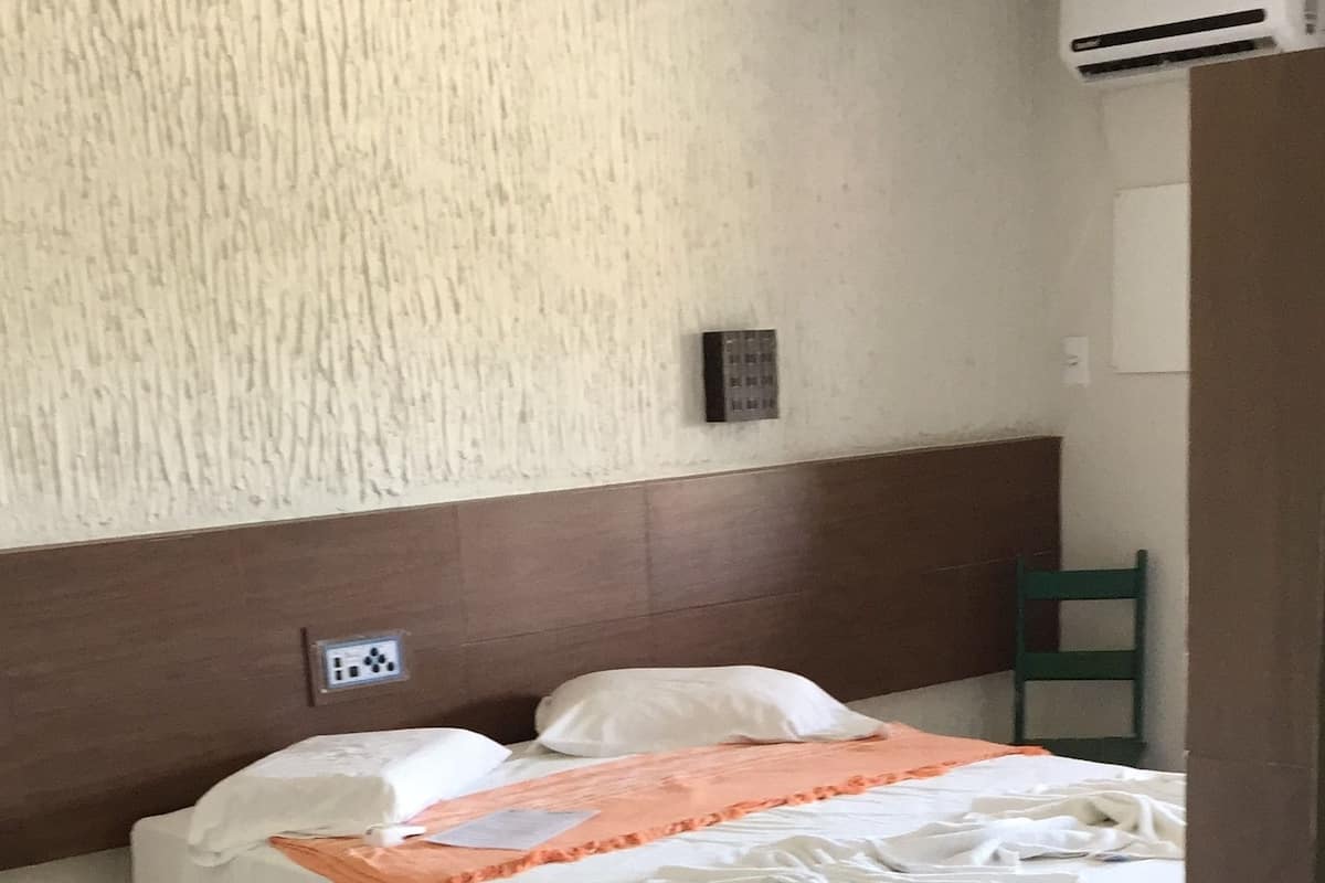 Hotellihuone, jossa on sänky, tuoli, pöytä ja ilmastointilaite.