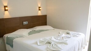 Een net opgemaakt bed met witte lakens en een groene deken, twee wandlampen en een bruin hoofdeinde.