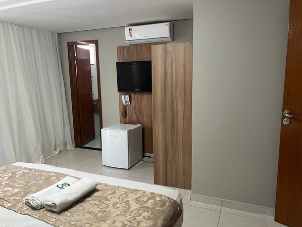 Una habitación de hotel con cama, refrigerador pequeño, teléfono y aire acondicionado.