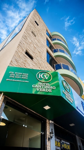 A hotel with a prominent green sign, a tall brick facade, and a circular balcony structure.